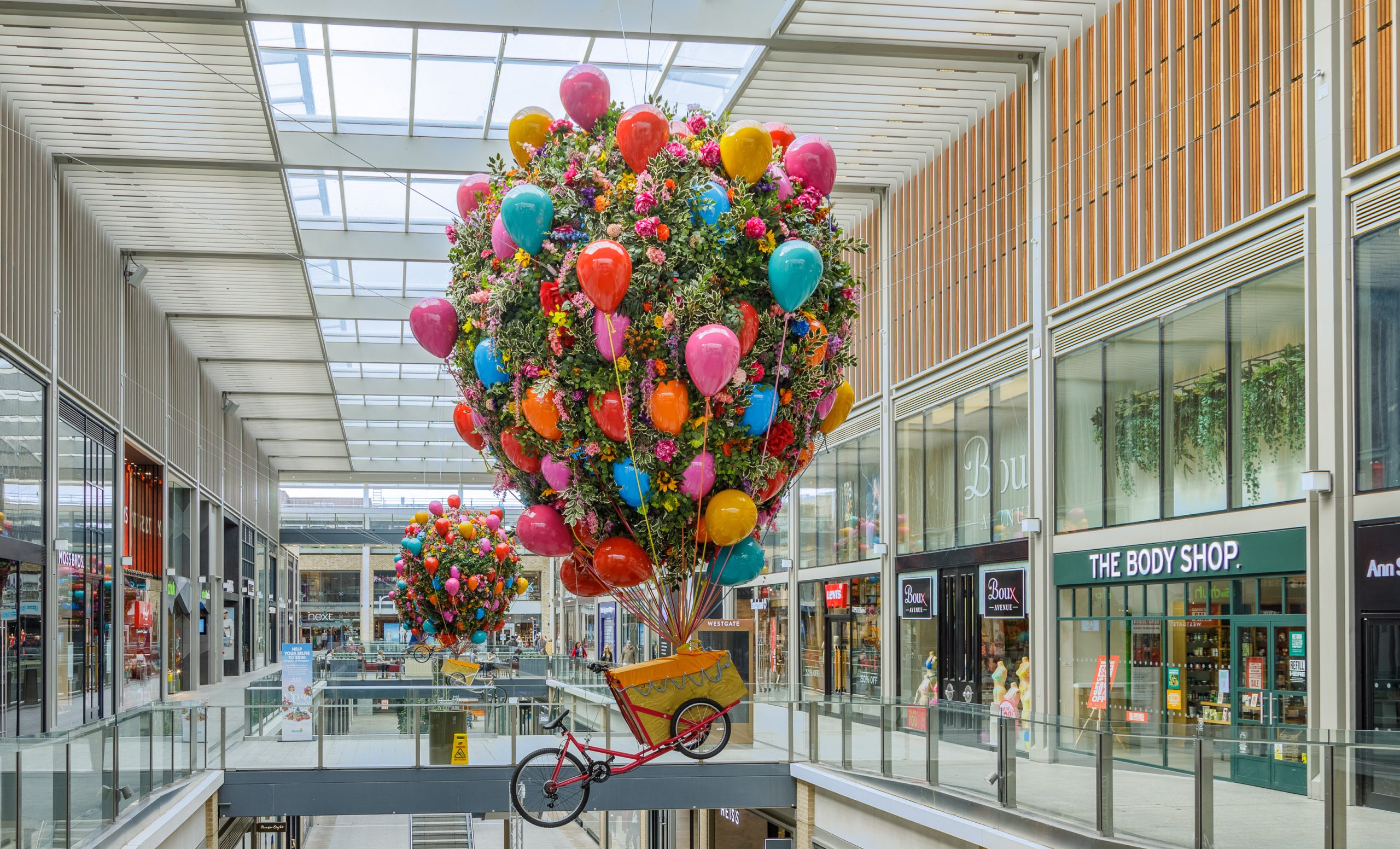 Giant flower-covered hot air balloon above a vintage bicycle in Westgate, Oxford